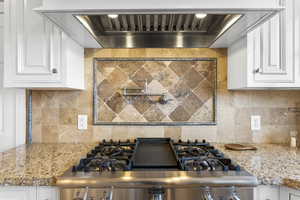 Kitchen view of white cabinetry, light stone counters, pot filler, and stainless steel gas stove