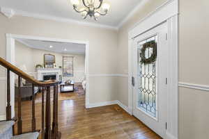 Foyer entrance with light wood finished floors, ornamental molding, hanging lights, and a lit fireplace