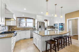 Kitchen with white cabinetry, light stone countertops, stainless steel appliances, pendant lighting, and a kitchen bar