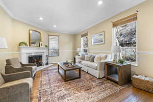 Living room featuring hardwood / wood-style flooring, a warm lit fireplace, crown molding, and recessed lighting