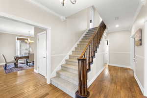 Staircase with a chandelier, ornamental molding, and wood-type flooring