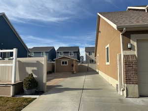 View of side of property with a residential view, a shed, stucco siding, and roof with shingles