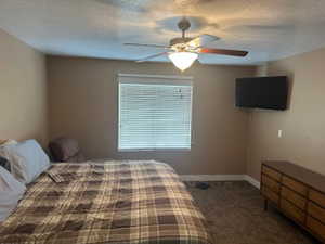 Bedroom with dark carpet, a ceiling fan, and a textured ceiling