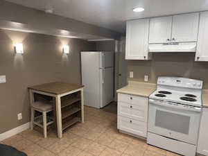 Kitchen with white appliances, white cabinetry, light countertops, and recessed lighting