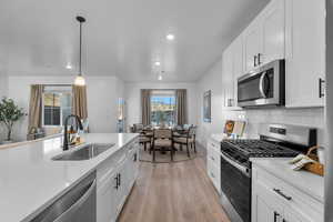 Kitchen featuring stainless steel appliances, white cabinets, light wood-type flooring, hanging light fixtures, and light stone counters