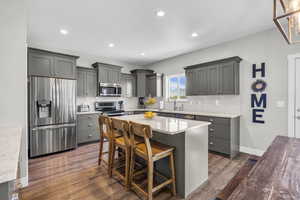 Kitchen featuring stainless steel appliances, gray cabinets, a breakfast bar area, light stone countertops, and a kitchen island