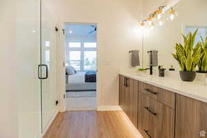 Ensuite bathroom featuring double vanity, light wood-style floors, and a stall shower
