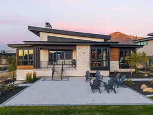 Back of house at dusk featuring a patio area, stone siding, and a chimney