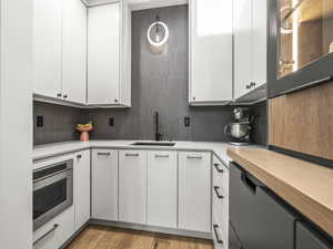 Kitchen with white cabinets, stainless steel oven, light wood-style flooring, and tasteful backsplash