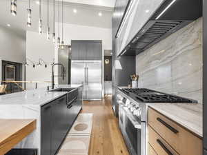 Kitchen with light stone counters, stainless steel appliances, modern cabinets, decorative light fixtures, and light wood-type flooring