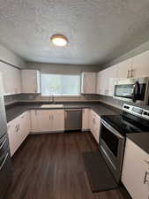Kitchen with dark countertops, stainless steel appliances, white cabinetry, a textured ceiling, and dark wood-type flooring