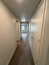Hallway with dark colored carpet and a textured ceiling