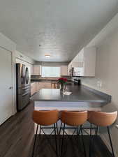 Kitchen with a peninsula, white cabinets, appliances with stainless steel finishes, a kitchen bar, and dark wood-type flooring