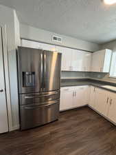 Kitchen with stainless steel fridge with ice dispenser, dark wood finished floors, white cabinetry, dark countertops, and a textured ceiling