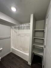 Full bathroom featuring shower / bathtub combination with curtain, dark wood-type flooring, and a textured ceiling