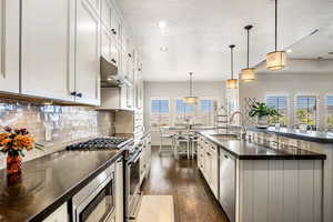 Kitchen with stainless steel appliances, dark wood-style flooring, pendant lighting, backsplash, and white cabinetry