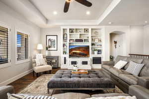 Living area featuring ceiling fan, a tray ceiling, wood finished floors, built in features, and arched walkways