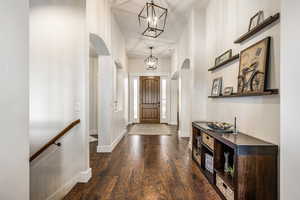 Foyer with arched walkways, dark wood finished floors, hanging lights, and a high ceiling