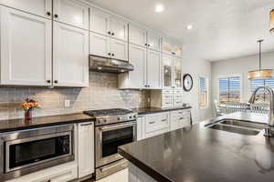 Kitchen featuring stainless steel appliances, decorative light fixtures, backsplash, dark stone counters, and a textured ceiling