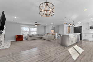 Living room featuring a ceiling fan, a brick fireplace, light wood-style floors, and suspended lighting