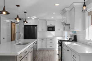 Kitchen featuring hanging light fixtures, a barn door, black appliances, light wood finished floors, and two tone cabinetry