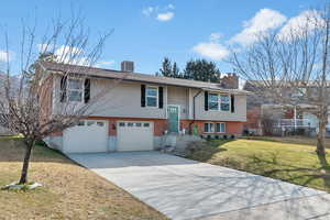 Bi-level home featuring brick siding, a garage, a front yard, driveway, and a chimney