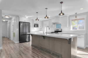 Two tone kitchen with stainless steel appliances, a kitchen bar, a center island with sink, hanging light fixtures, and dual tone cabinetry