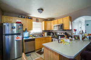 Kitchen featuring stainless steel appliances, a peninsula, a breakfast bar, a textured ceiling, and arched walkways