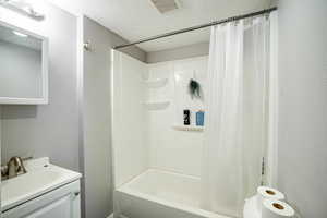 Bathroom with a textured ceiling, shower / bath combo with shower curtain, a textured wall, and vanity