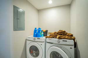 Laundry room with electric panel, washing machine and dryer, a textured wall, and recessed lighting