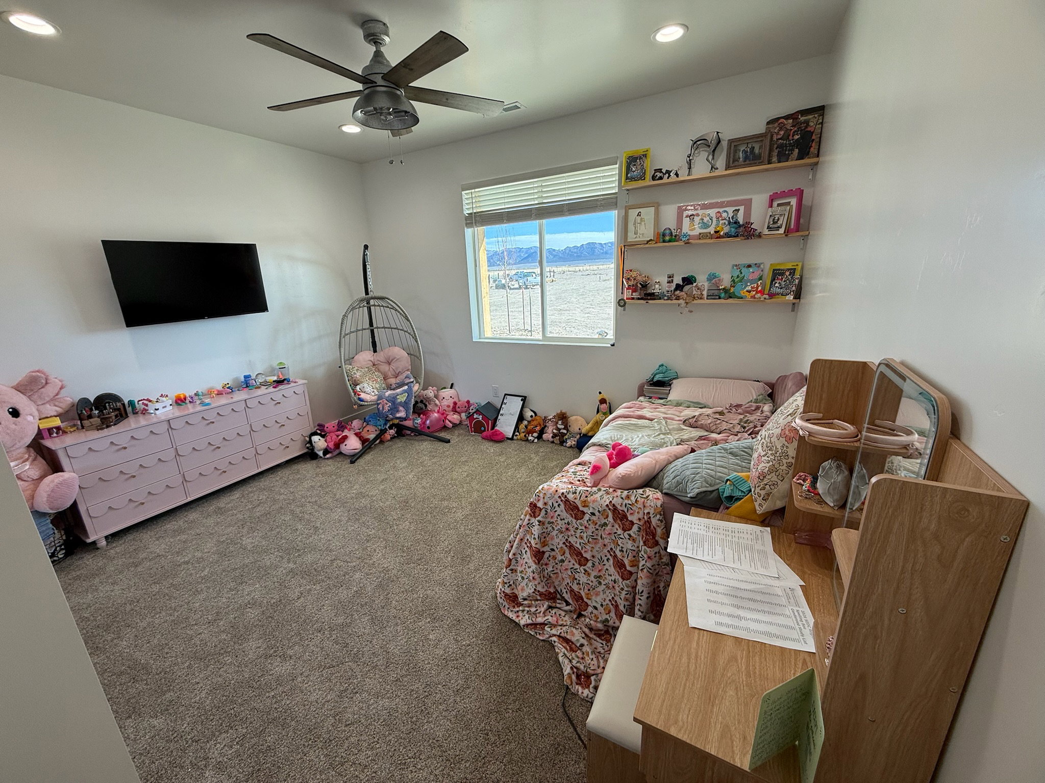 Carpeted interior room featuring a ceiling fan with integrated lighting, recessed ceiling lights, and a window with blinds