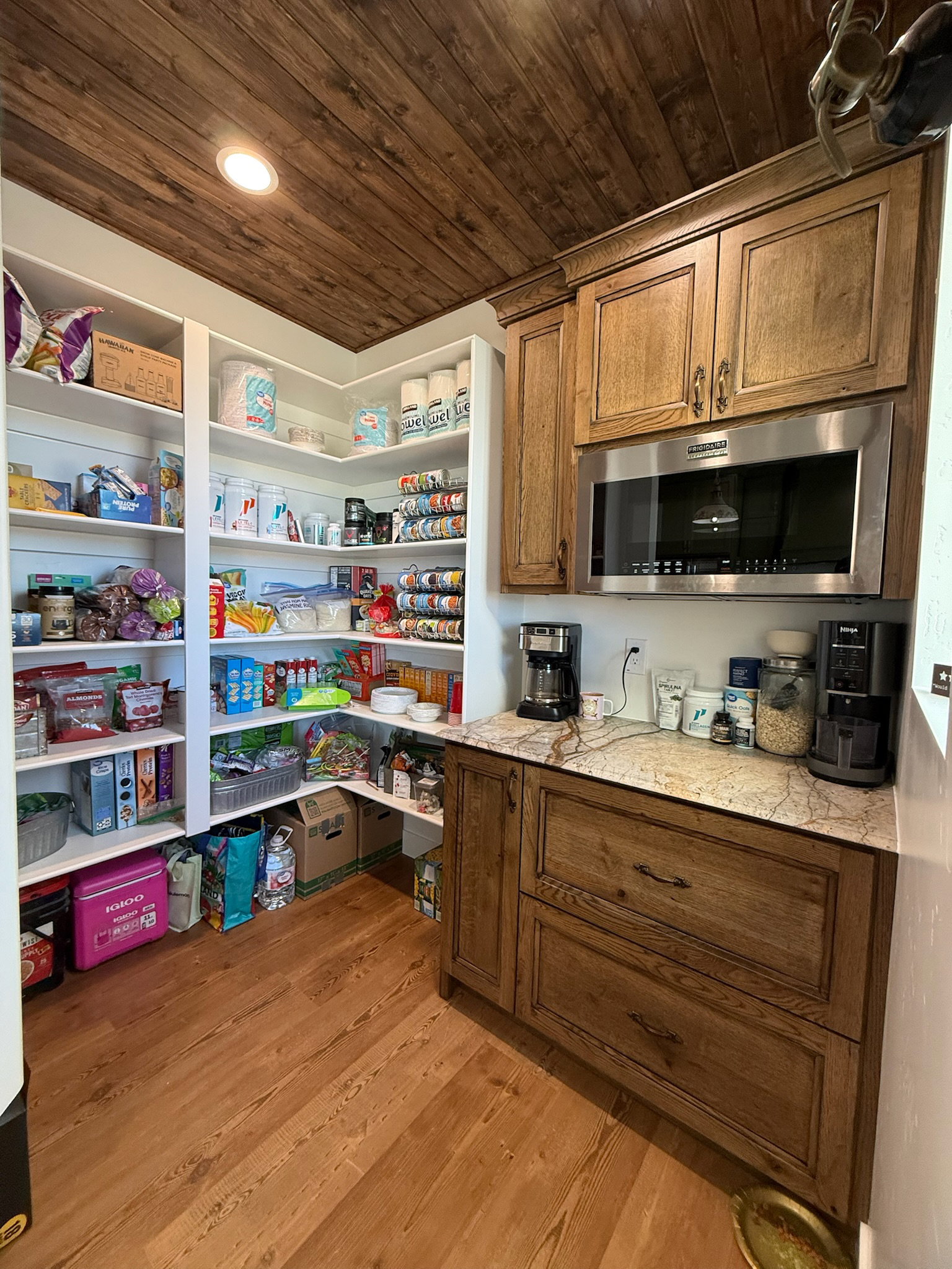 Spacious pantry featuring extensive built-in shelving, wood-finish flooring, a wood plank ceiling, custom wood cabinetry, and a stainless steel microwave