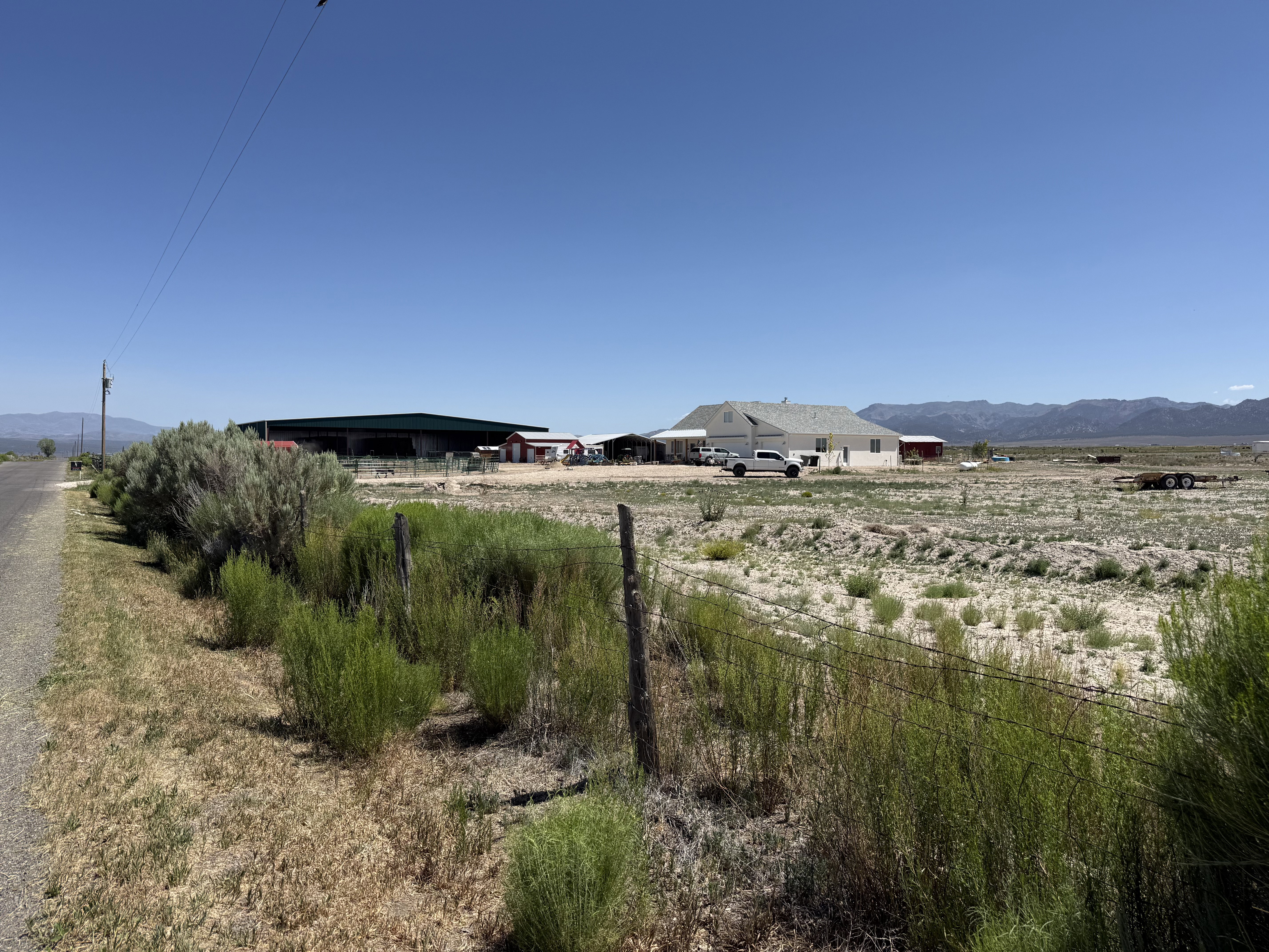 Rural property featuring a white ranch-style home, multiple outbuildings, and expansive undeveloped land