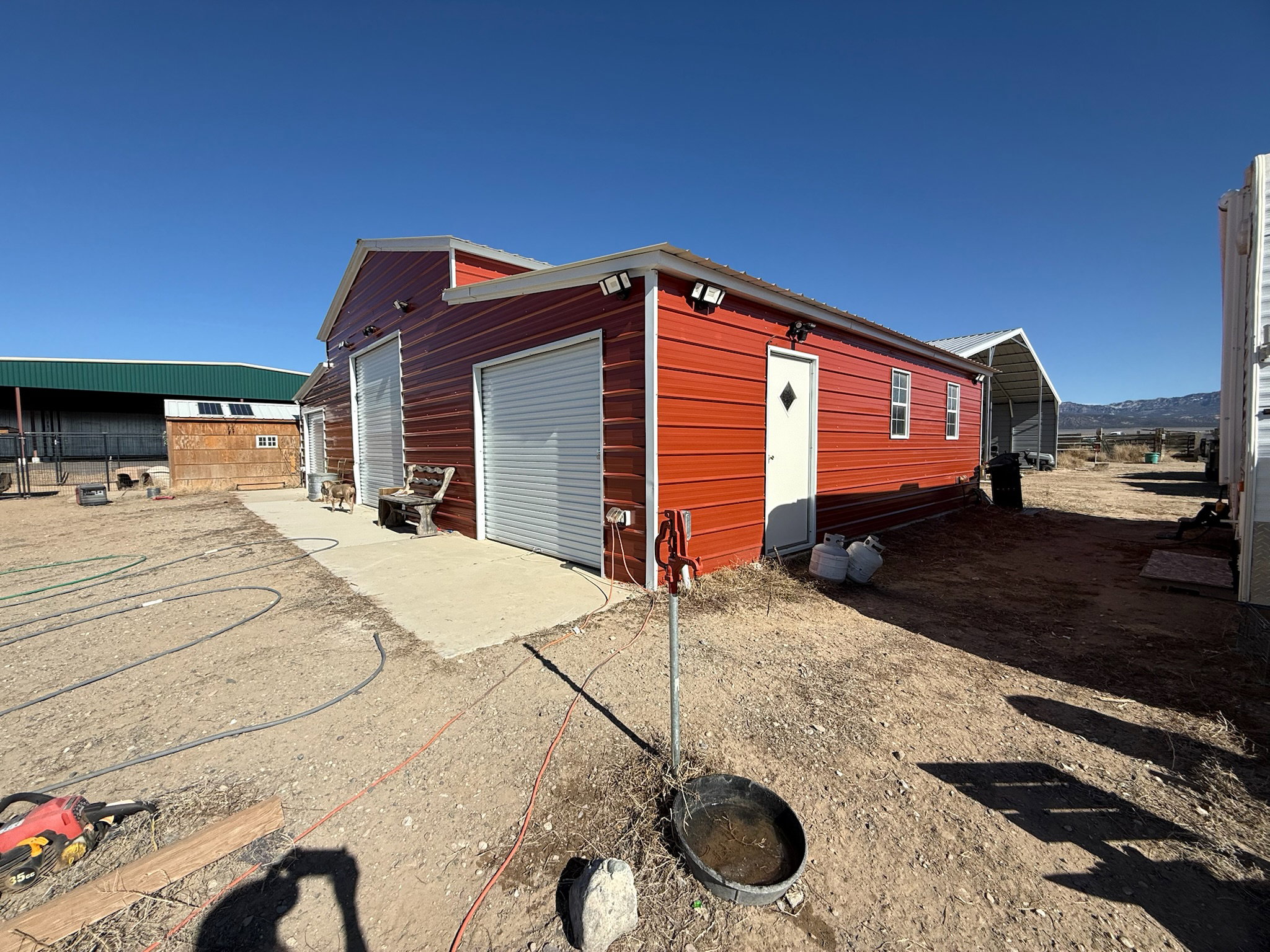 Red metal-sided structure featuring multiple roll-up garage doors, a pedestrian entrance, and exposed exterior lighting