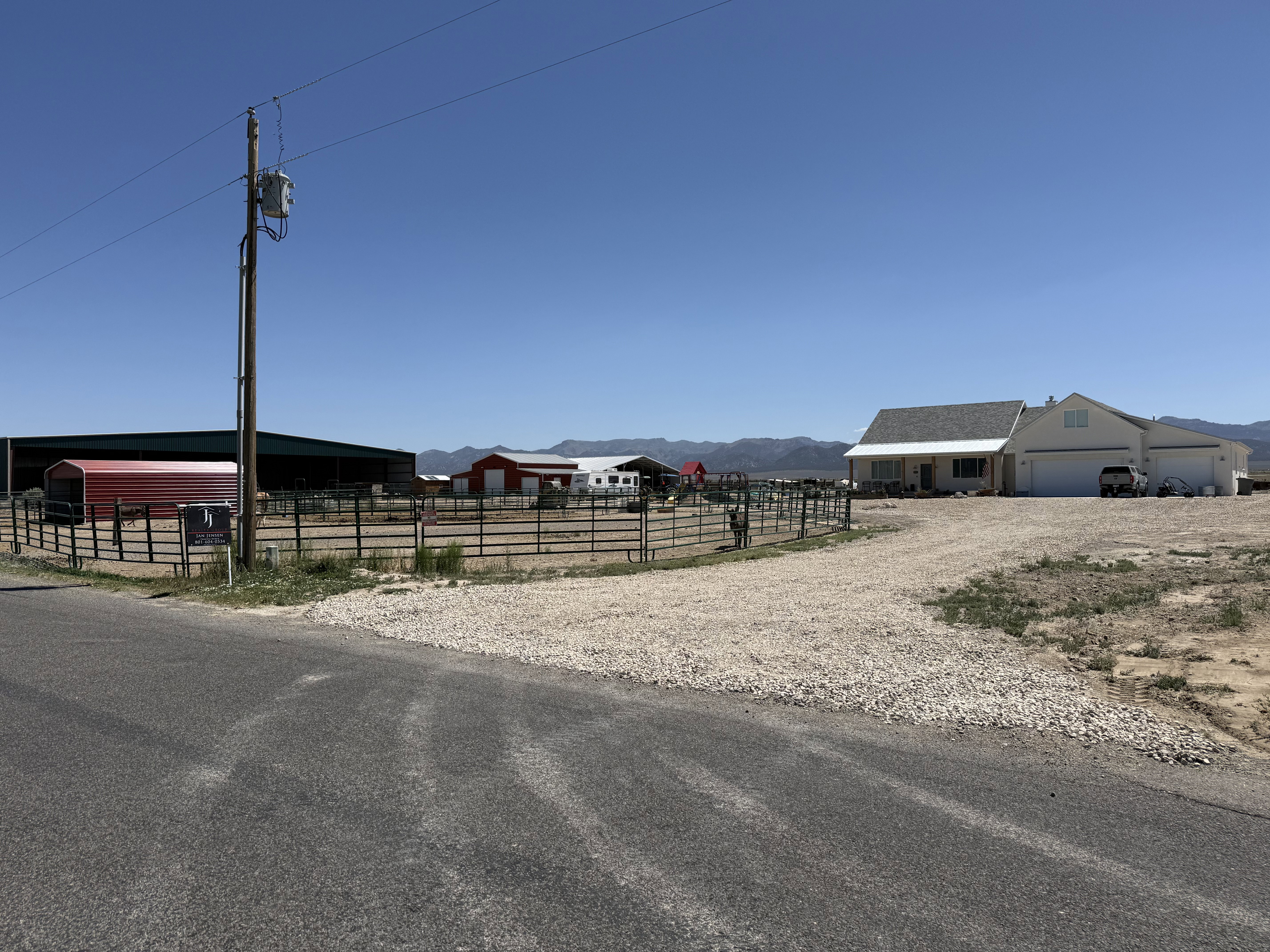 Expansive property featuring a modern ranch-style home with an attached garage, gravel driveway, and multiple outbuildings including a large barn and red-sided structures