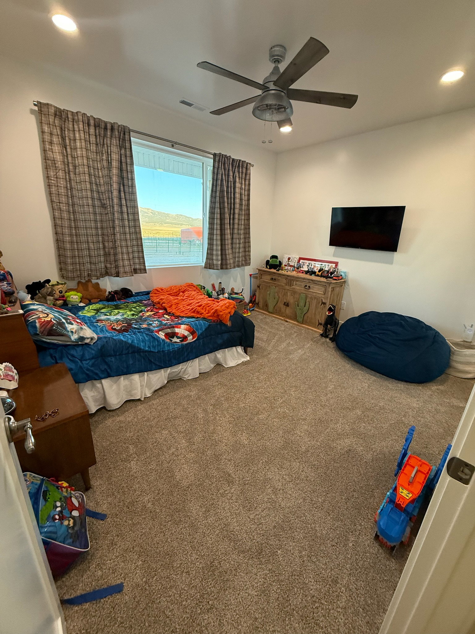 Spacious room featuring neutral carpeting, a large window, and a ceiling fan with integrated lighting