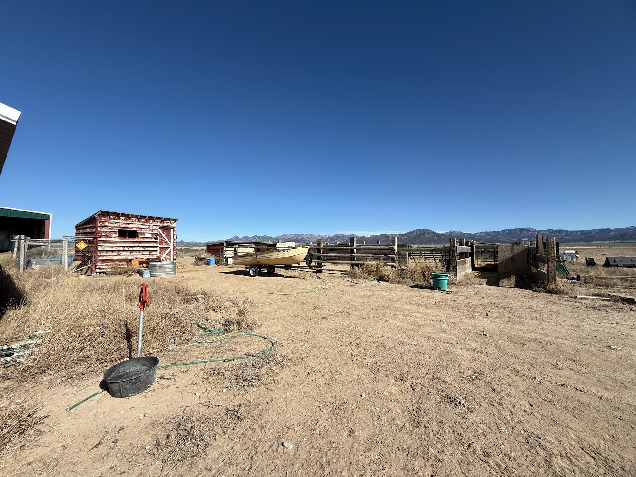 Expansive outdoor area featuring a rustic red-painted storage shed, a large green metal building, and extensive wooden fencing
