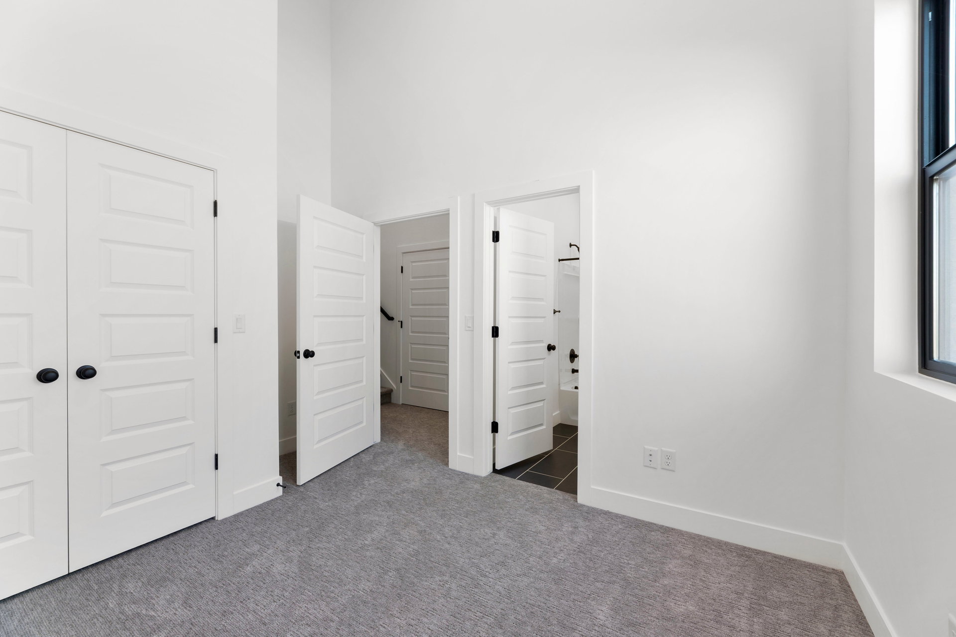 Unfurnished bedroom featuring ensuite bath, a high ceiling, a closet, and dark carpet