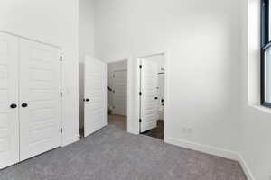 Unfurnished bedroom featuring ensuite bath, a high ceiling, a closet, and dark carpet