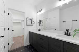 Bathroom featuring double vanity, a spacious closet, dark colored carpet, and dark tile patterned floors
