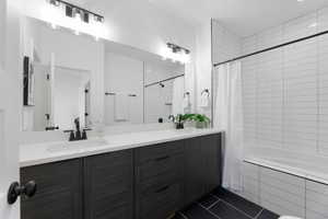 Full bath featuring vanity, tiled shower / bath, and dark tile patterned flooring