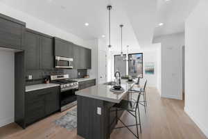 Kitchen with stainless steel appliances, a breakfast bar area, a center island with sink, light wood finished floors, and modern cabinets