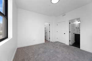 Unfurnished bedroom with dark colored carpet, a closet, and ensuite bath