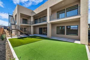 Rear view of house with stucco siding, a patio area, a lawn, and a balcony