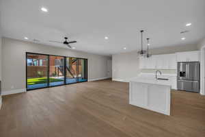 Kitchen featuring stainless steel fridge, white cabinets, a center island with sink, open floor plan, and hanging light fixtures