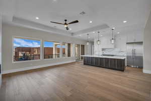 Kitchen with dual tone cabinetry, open floor plan, a raised ceiling, stainless steel built in fridge, and a spacious island