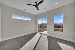 Spare room with dark colored carpet, a ceiling fan, and plenty of natural light
