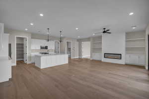 Kitchen featuring white cabinets, hanging light fixtures, open floor plan, a ceiling fan, and a fireplace