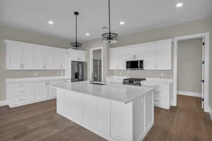Kitchen with white cabinetry, stainless steel appliances, dark wood-style floors, an island with sink, and decorative light fixtures