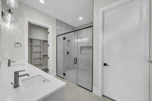 Full bath with a walk in closet, a shower stall, double vanity, concrete floors, and recessed lighting